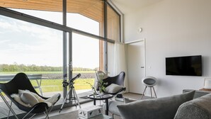 A modern living room with a large window, a telescope, a flat-screen TV, and a cozy seating area. - Beautiful nature house with terrace by the water (Wissenkerke)
