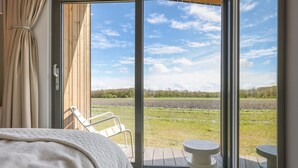 A bedroom with a bed, a chair, and a table by a large window overlooking a field. - Beautiful nature house with terrace by the water (Wissenkerke)