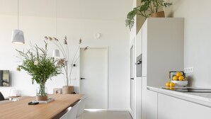 A modern kitchen with white cabinets, a wooden dining table, and a countertop with a bowl of fruit. - Beautiful nature house with terrace by the water (Wissenkerke)