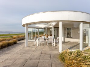 Uma estrutura moderna de vidro curvo com área de pátio, assentos externos e vista para o mar.