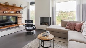 Una sala de estar moderna con un televisor de pantalla plana, un sillón de cuero, un sofá, una chimenea y un ventanal con cortinas.