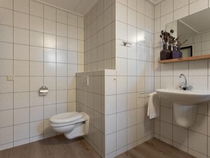 A bathroom with white tiled walls, a toilet, a sink, and a mirror above the sink. - Family villa near Lake Veere with garden (Kamperland)