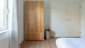 A bedroom with a bed, a wardrobe, a window with curtains, a door, and a wall-mounted hook. - Holiday home on Lake Veere (Kamperland)