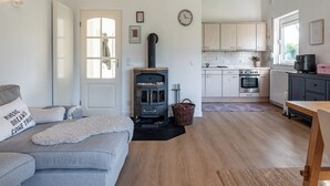 A cozy living room with a grey sofa, a fireplace, a kitchen with light wooden cabinets, and a dining area. - Holiday home on Lake Veere (Kamperland)