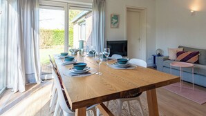 A dining area with a long wooden table, blue plates, and wine glasses, a television, and a sofa. - Holiday home on Lake Veere (Kamperland)