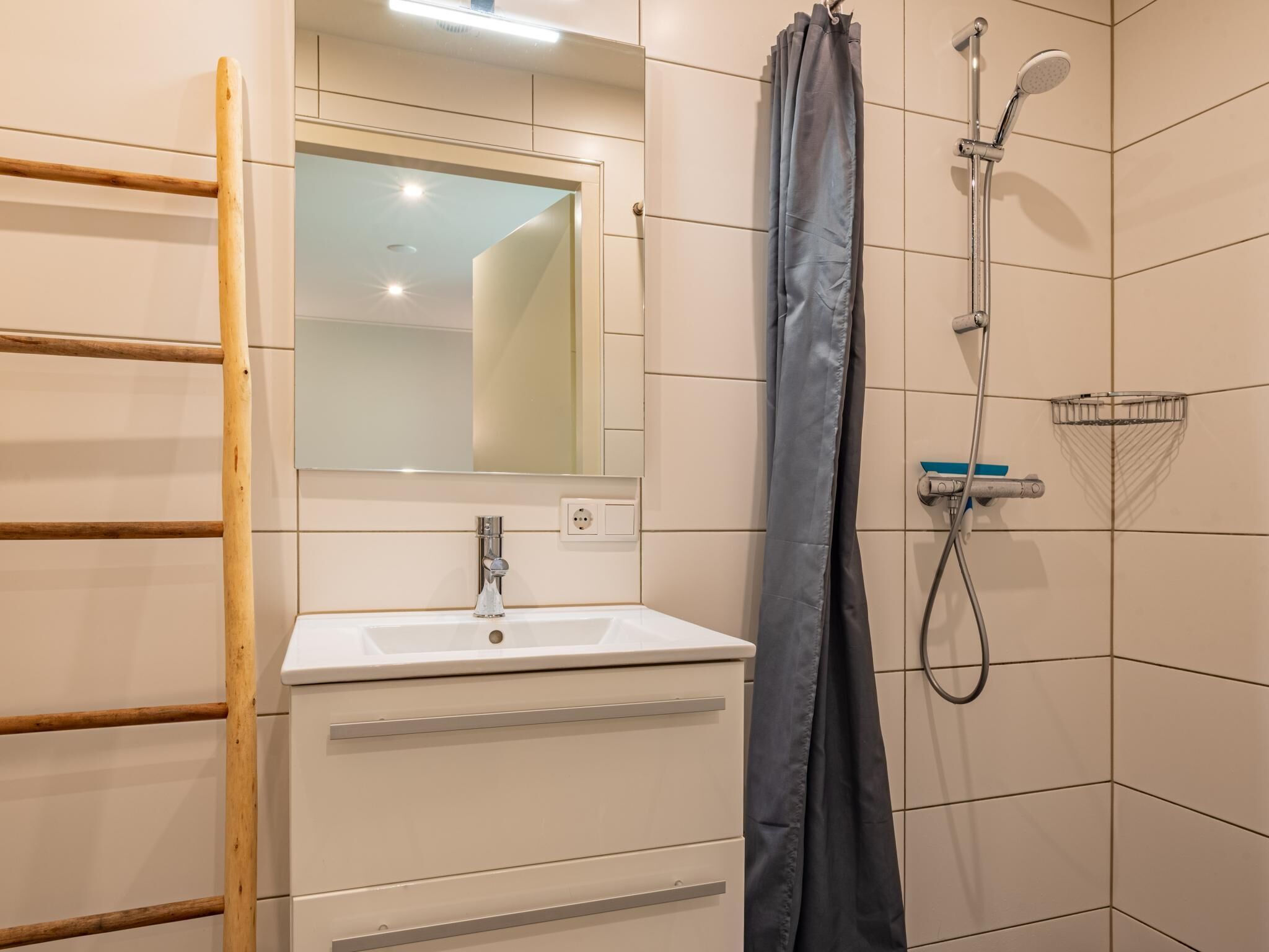 Ein Badezimmer mit einer Holzleiter, einem Waschbecken, einem Spiegel, einer Dusche mit Duschbrause und gefliesten Wänden.