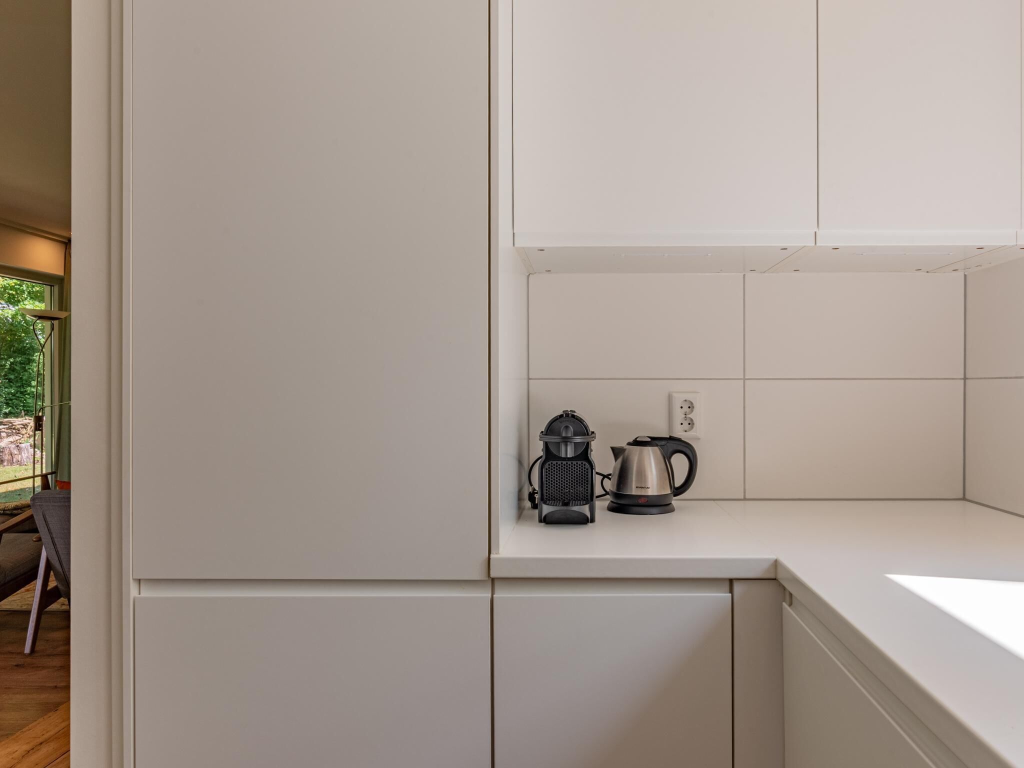 A modern kitchen with white cabinetry, a kettle, and a coffee maker on the countertop.