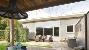 Eine Terrasse im Freien mit einem Holztisch, Korbstühlen und einer hängenden Lampe.