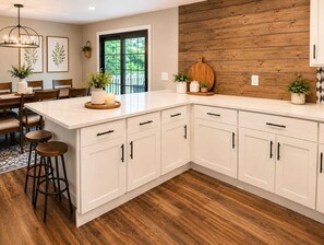 Eine Küche mit weißen Schränken, einer Holzausziehtafel und einem Essbereich mit Tisch und Stühlen.