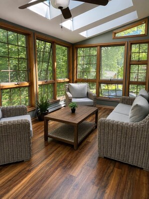 Ein Wintergarten mit großen Fenstern, Korbmöbeln und einem Deckenventilator.