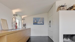 Una cocina moderna con encimera de madera, pileta de acero inoxidable y un cuadro con un faro en la pared.