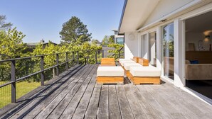Terraza de madera con mobiliario exterior, puerta de cristal que da a una habitación y vistas despejadas del entorno verde.