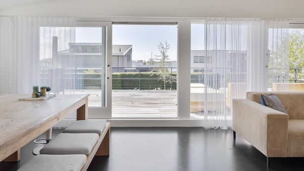 Un espacio habitable moderno con una mesa de comedor de madera, un sofá y un ventanal corredero que da a un área exterior.