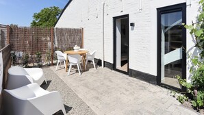 A white brick building with a patio area featuring a table and chairs, a wooden door, and a window. - Nice, light apartment with a terrace. (Kamperland)