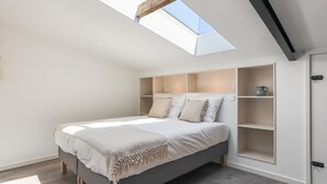 A modern bedroom with a skylight, built-in shelving, and a bed with a grey headboard. - Nice, light apartment with a terrace. (Kamperland)