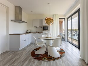 A modern kitchen with white cabinets, a microwave, and a stove. There is a dining area with a round table and white chairs. - Design Apartment Port of Kamperland (Kamperland)