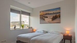 Ein Schlafzimmer mit zwei Betten, einem Fenster mit Blick auf Gebäude und einem Bild an der Wand.