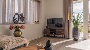 Ein modernes Wohnzimmer mit Fernseher, Holzmöbeln, Kamin und einem großen Fenster mit Vorhängen.
