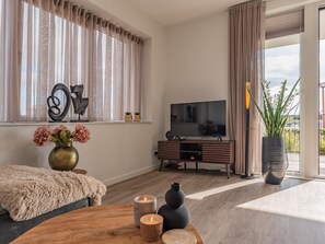 A modern living room with a TV, wooden furniture, a fireplace, and a large window with curtains. - Harbour Apartment with Terrace Kamperland (Kamperland)