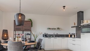 Eine moderne Küche mit weißen Schränken, einem Essbereich mit Holztisch und -stühlen sowie Pendelleuchten.