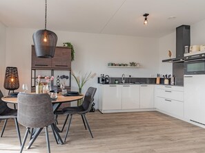 A modern kitchen with white cabinets, a dining area with a wooden table and chairs, and pendant lighting. - Harbour Apartment with Terrace Kamperland (Kamperland)