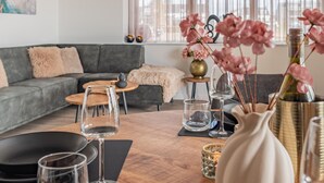 Ein modernes Wohnzimmer mit einem grauen Sofa, einem Holztisch und einer Vase mit rosa Blumen.