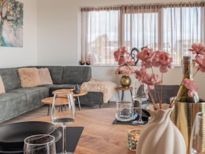 A modern living room with a grey sofa, a wooden coffee table, and a vase with pink flowers. - Harbour Apartment with Terrace Kamperland (Kamperland)