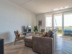 A modern living room with a sofa, a television, and a large window offering a view of the sea. - Luxury apartment right by the marina (Kamperland)