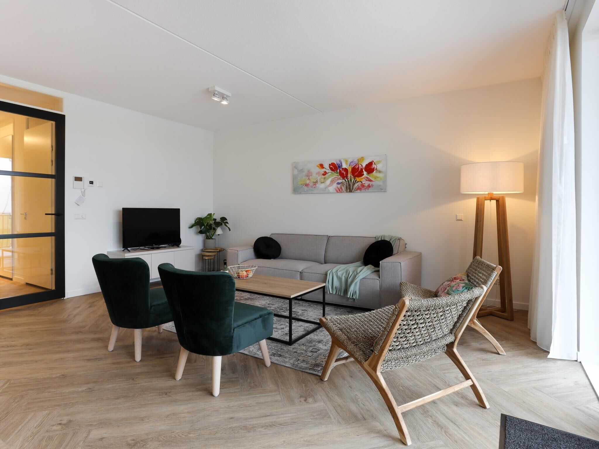 Een moderne woonkamer met een bank, twee stoelen, een salontafel, een televisie, een schilderij en een vloerlamp.