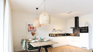 Una cocina moderna con armarios blancos, una estufa negra y un comedor con mesa y sillas de madera.