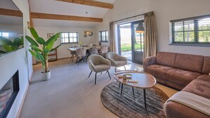 A spacious living area with a high ceiling, wooden beams, a dining table with chairs, a sofa, and a large window with curtains.