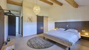 A modern bedroom with a large bed, a round rug, a hanging light fixture, and a wooden ceiling.
