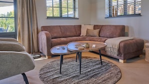 A living room with a brown sofa, a round coffee table, a lamp, and two windows with blinds.