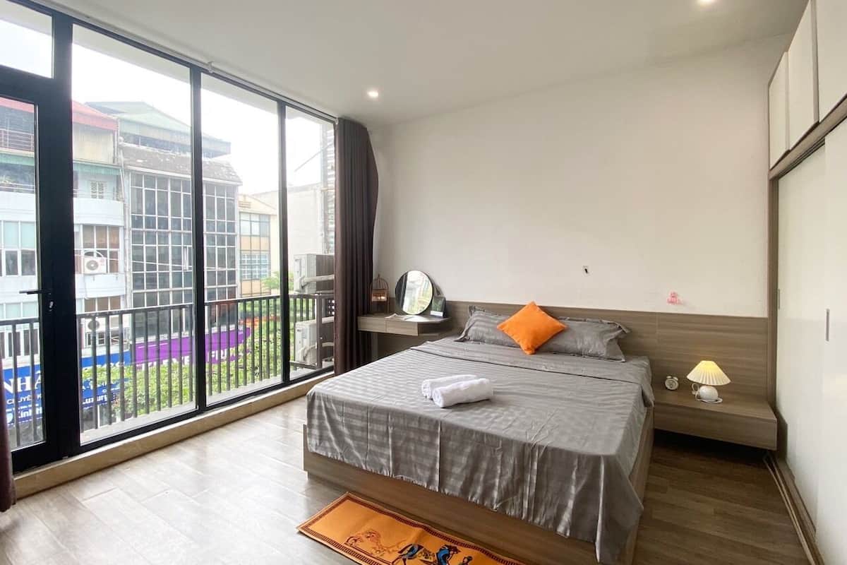 Een moderne hotelkamer met een groot bed, een nachtkastje met lamp, een raam met uitzicht op gebouwen, en een balkon.