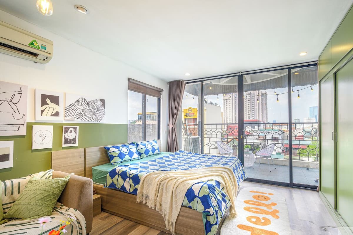 Een slaapkamer met een bed, een slaapbank, een balkon met uitzicht en kunst aan de muur.