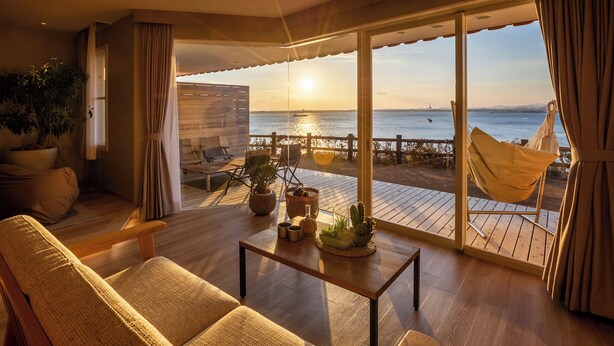 Un balcón amplio con vistas al mar, una hamaca y un área de descanso con mesa y plantas.