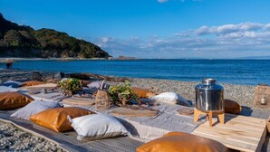 Un paisaje de playa con una mesa dispuesta para una comida, un recipiente metálico y una cesta de mimbre.
