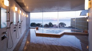 Un spa moderno con un ventanal grande, una bañera de hidromasaje y múltiples cabezales de ducha.