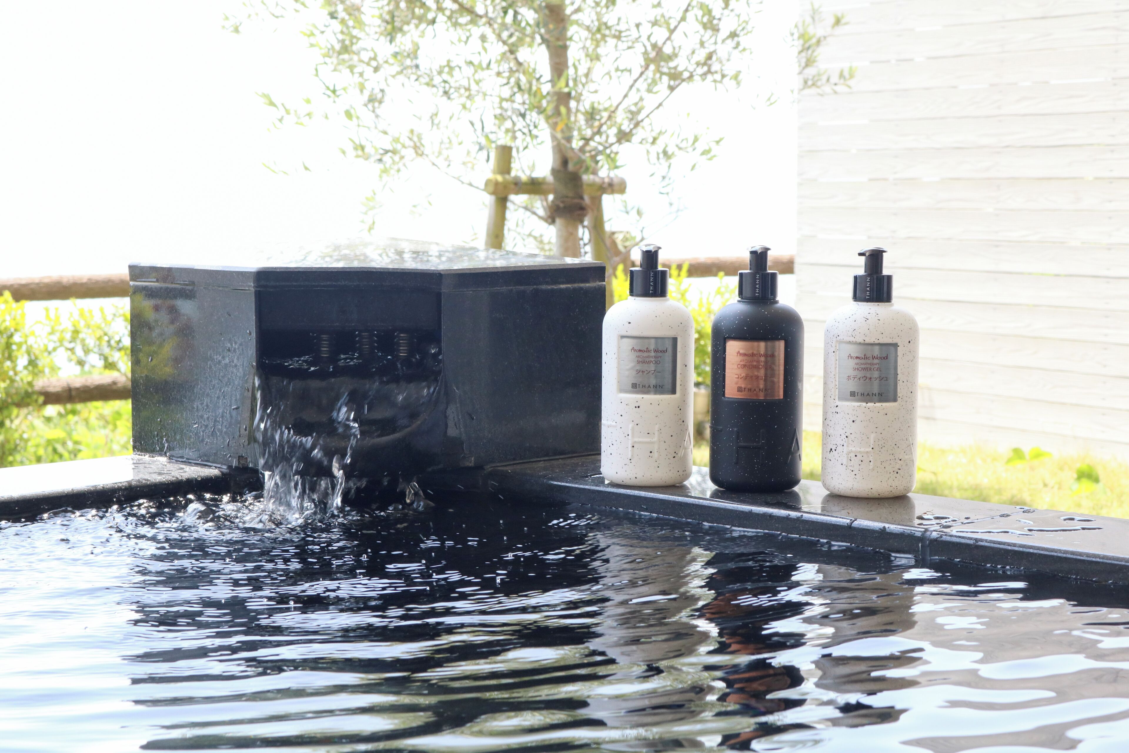 Una bañera de hidromasaje con agua corriendo, rodeada por tres botellas de productos de cuidado corporal.
