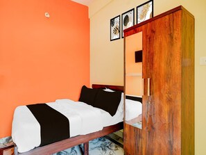 A room with a bed, a wooden wardrobe, and a wall with framed artwork. - Deluxe Nataraja Boarding & Lodging (Bengaluru)