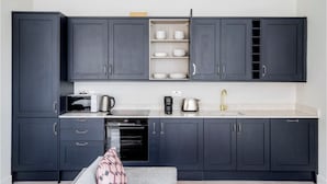 Une cuisine moderne avec des meubles de couleur sombre, un four à micro-ondes, une machine à café, un grille-pain et un évier doté d’un robinet doré.
