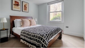 Un lit bien fait, recouvert d’une couvre-lit à motifs, avec deux lampes de chevet et deux œuvres d’art encadrées accrochées au mur.