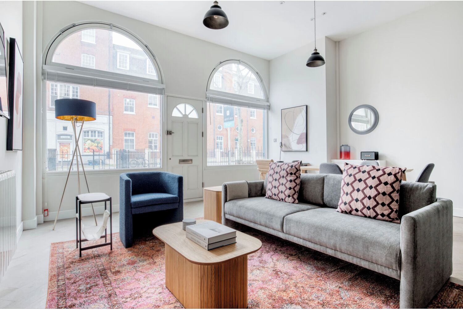 Ein modernes Wohnzimmer mit einem grauen Sofa, einem blauen Sessel, einem Couchtisch und einem großen Fenster mit Blick auf Gebäude.