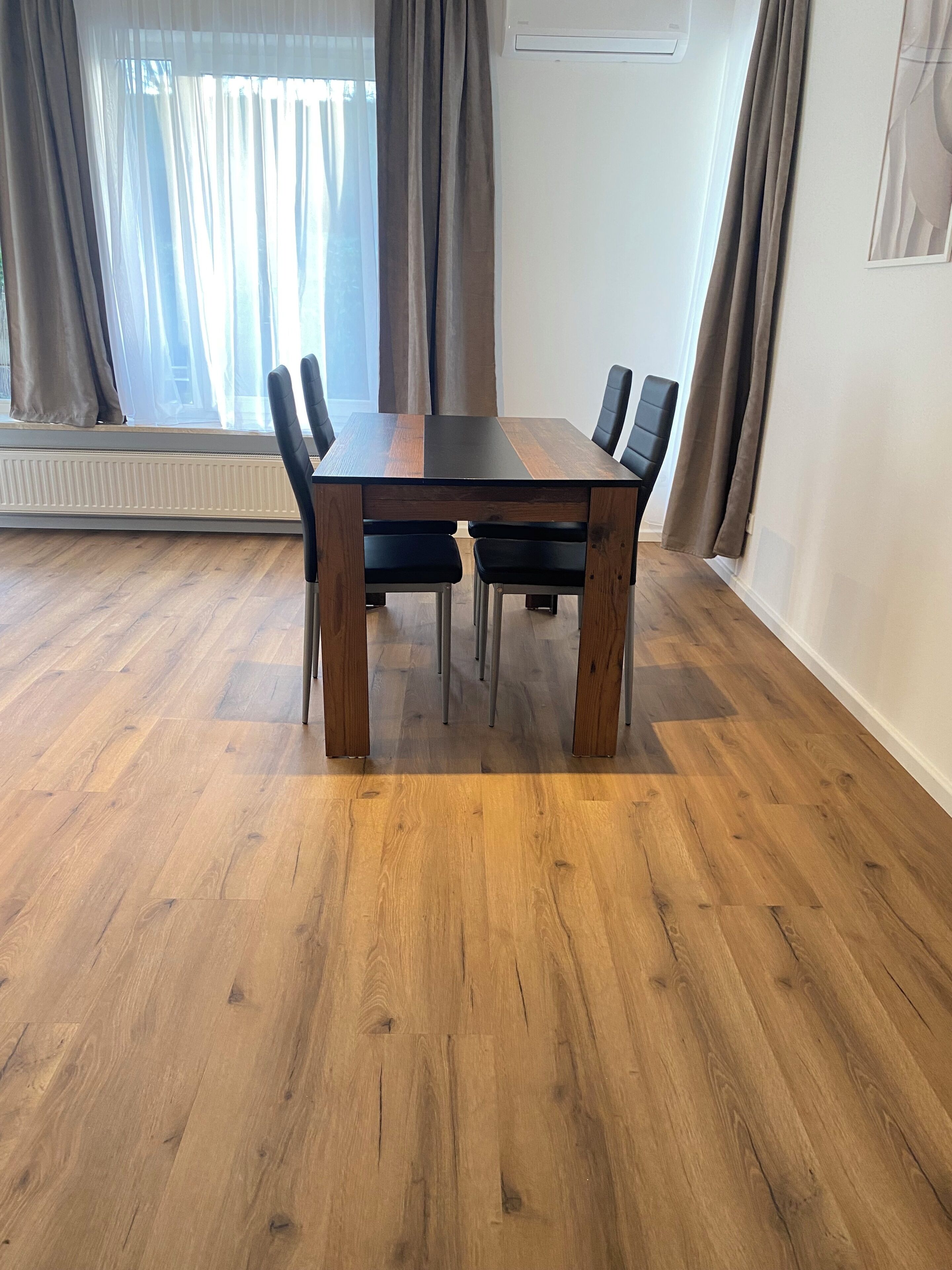A dining table with chairs, a radiator, and curtains.