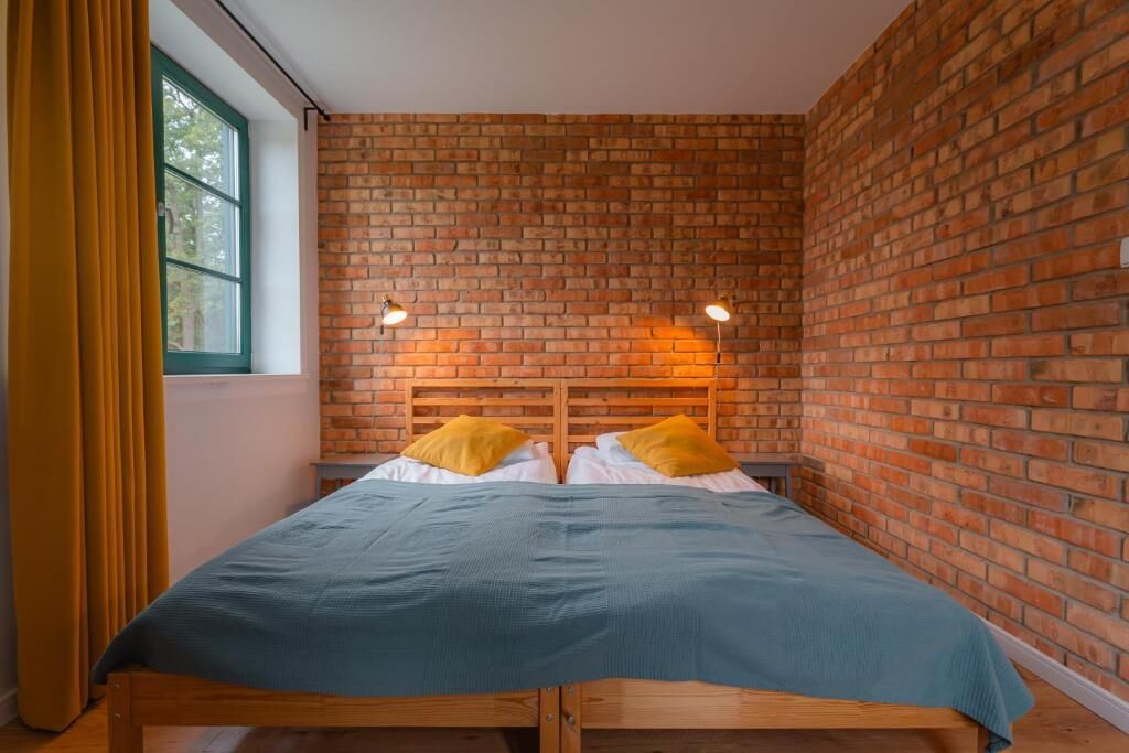 Een enkel bed met houten frame, een bakstenen muur en twee bedlampjes.