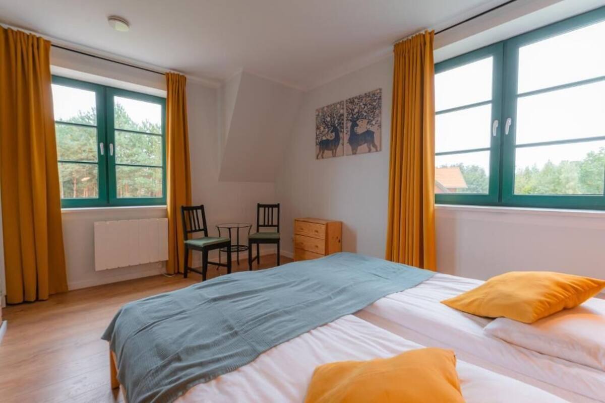Une chambre à coucher comprenant un lit, deux chaises, une petite table, une commode et une fenêtre avec des rideaux.