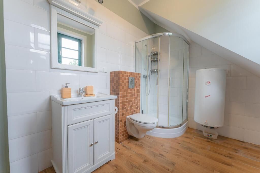 Een badkamer met een wit wastafelmeubel, een douchecabine met glazen wanden, een wit toilet en een boiler.