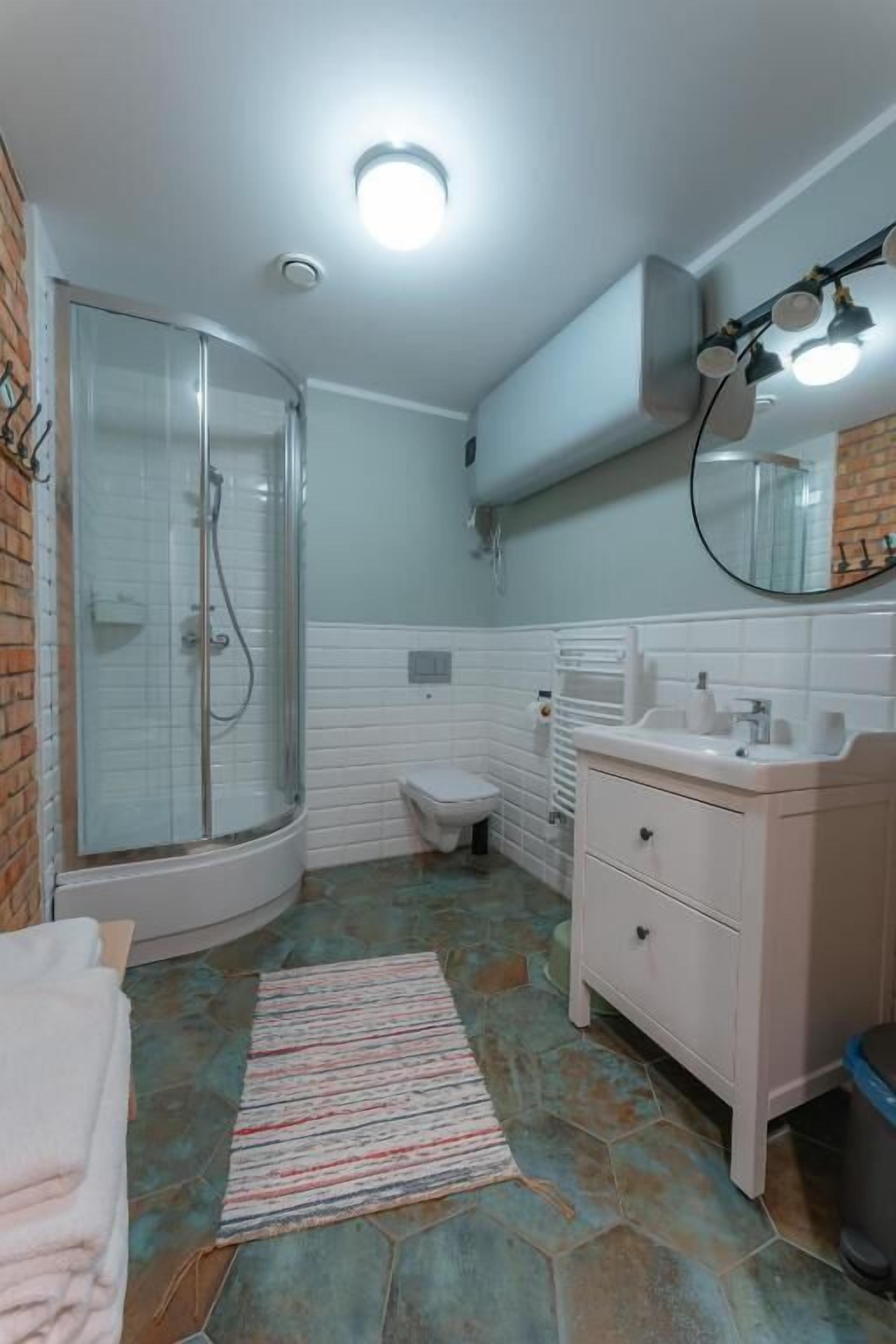 Ein Badezimmer mit Duschkabine aus Glas, einem weißen Waschbecken, einer Toilette und einem gemusterten Teppich.
