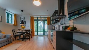 A modern kitchen with wooden cabinets, a dining area with a table and chairs, and a large window with curtains. - Mazurskie Domy Nad Kisajnem (Giżycko)