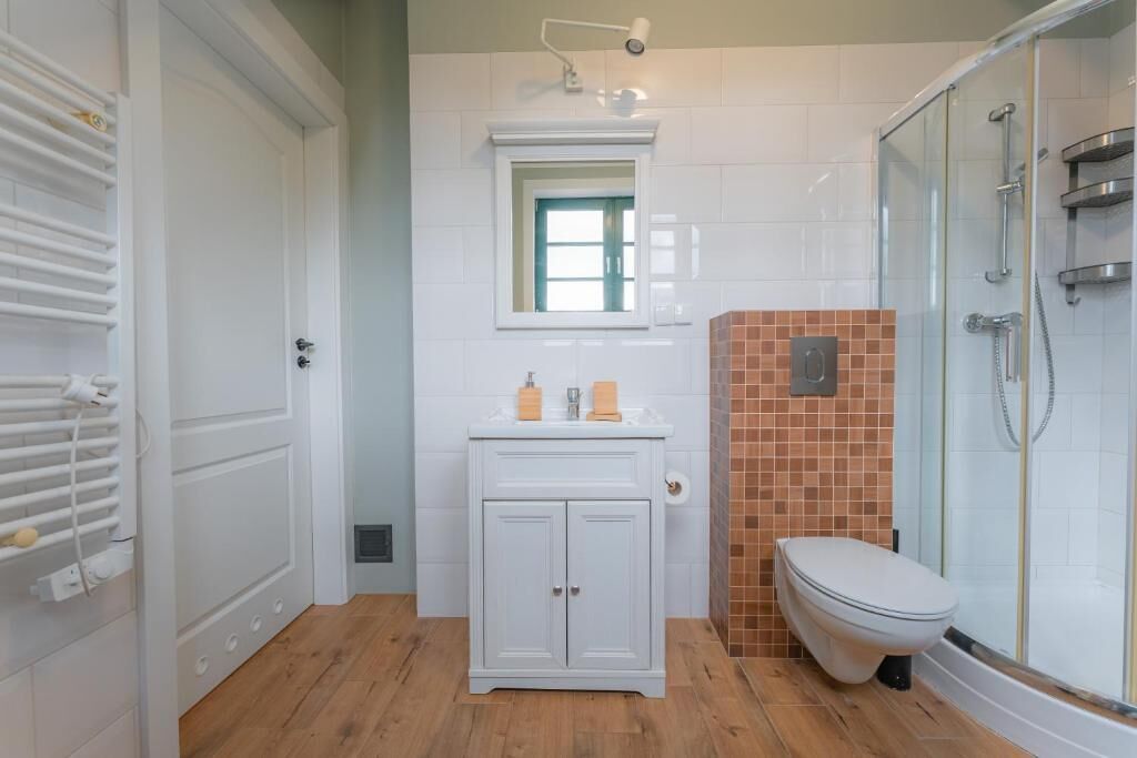 A bathroom with a white vanity, a toilet, a glass shower enclosure, and a window above the vanity.